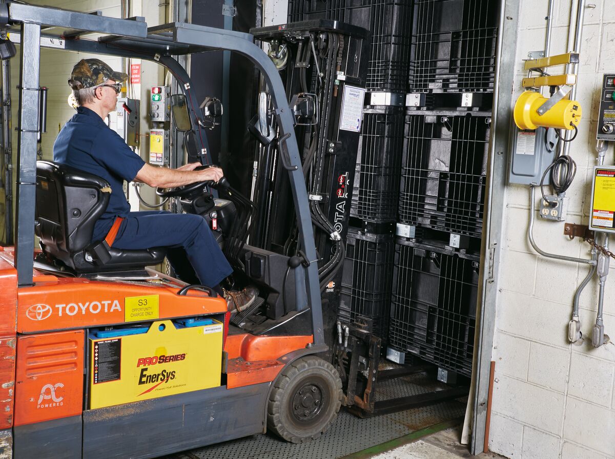 Worker operating a Toyota forklift, loading shelves into a large metal compartment in an industrial setting.